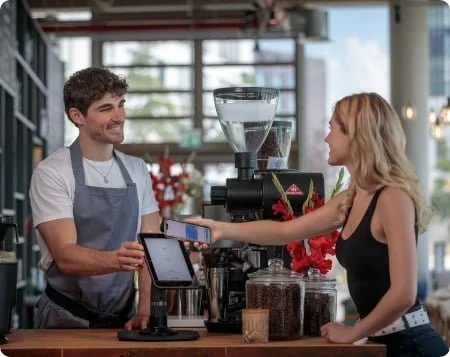 Tap to pay sdk use case for retail, lady in a cafe uses tablet pos system, customer in a cafe pays with their phone on a pos tablet